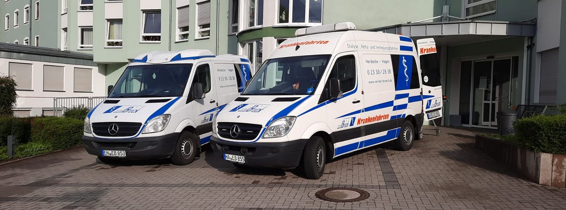 Zwei weiße und blaue Krankenwagen stehen vor einem Gebäude geparkt.